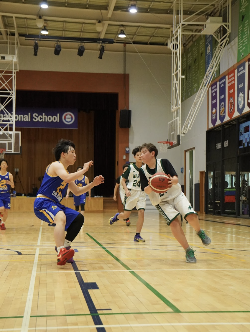 Sixth grader Aiden Hwang (21) drives toward the basket with determination, keeping control under defensive pressure. His energy pushes the Jets' offense forward against the Dragons. 